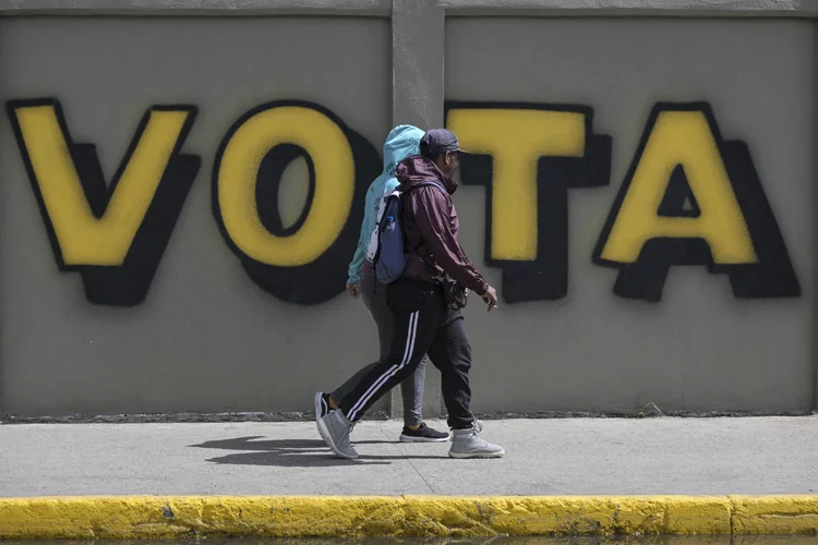 Um casal passa por um grafite na parede que diz “vote”, em meio às eleições presidenciais na Venezuela, em Caracas, em 27 de julho de 2024 (AFP/AFP Photo)