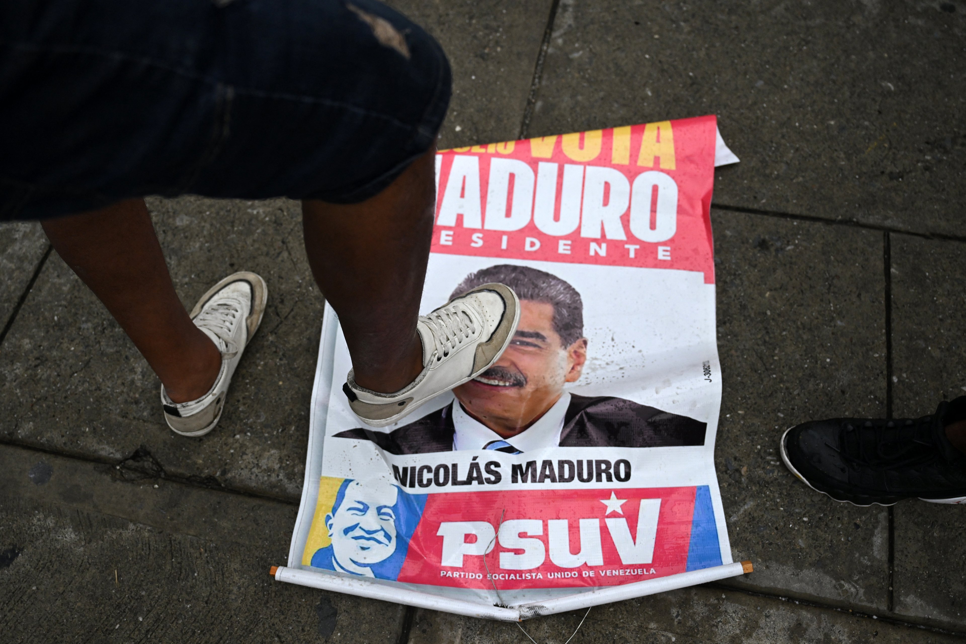 Opositor ao governo pisa num cartaz de campanha eleitoral com a imagem de Maduro durante um protesto no bairro Petare, em Caracas, na segunda-feira