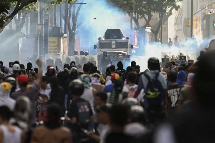 Manifestantes entram em confronto com a polícia perto de um carro blindado da polícia durante um protesto contra o presidente venezuelano Nicolás Maduro em Caracas. (Federico Parra/AFP)