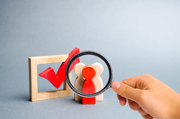 Magnifying glass is looking at the people stand near the checkbox for voting in elections. Lobbying interests, election corruption, voter bribery, and rigging election results. Selective focus (AdobeStock/Reprodução)