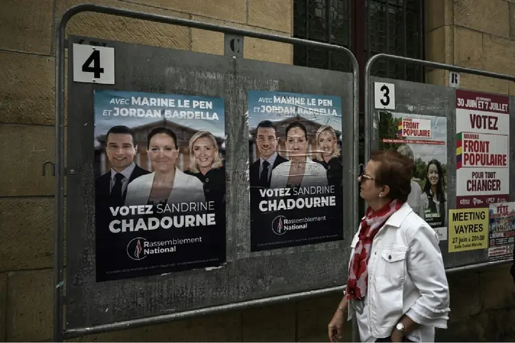 Mulher passa por alguns cartazes eleitorais das eleições legislativas francesas, em 2 de julho de 2024, em Libourne, sudoeste da França (AFP)