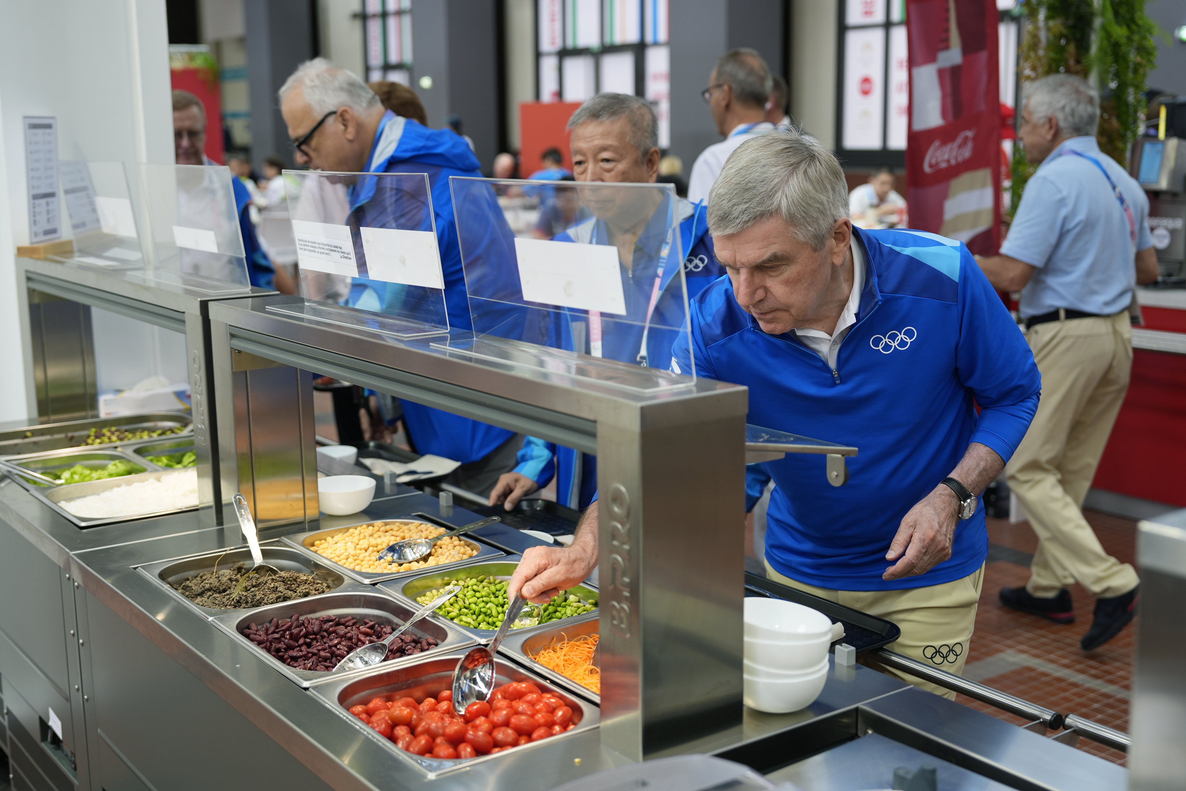 O presidente do COI, Thomas Bach, experimenta comida de um bufê de saladas enquanto visita a Vila Olímpica antes do início dos Jogos Olímpicos de Paris 2024
