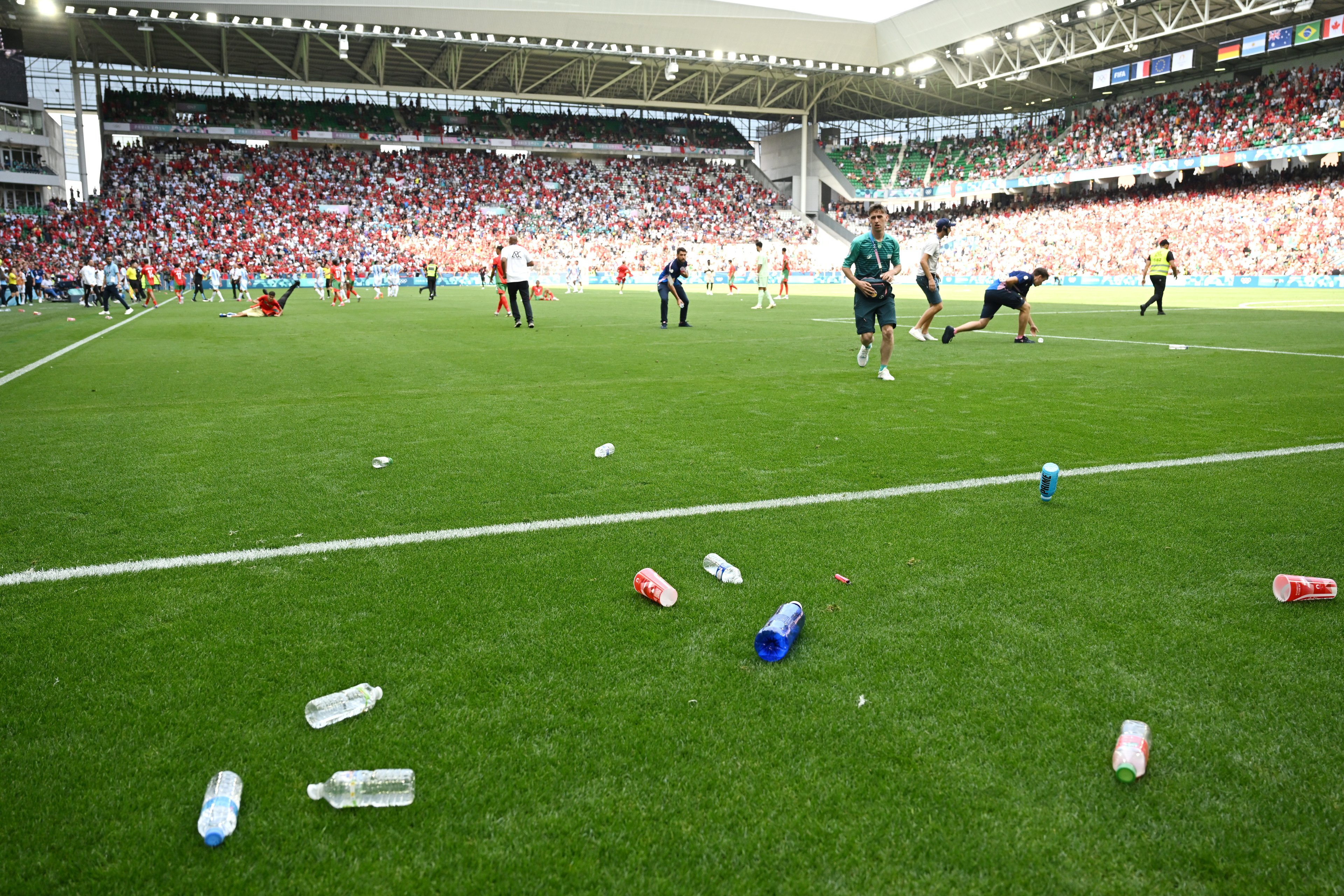Uma visão geral dentro do estádio enquanto a equipe remove garrafas do campo que foram atiradas das arquibancadas durante a partida do grupo B masculino entre Argentina e Marrocos durante os Jogos Olímpicos de Paris 2024 no Stade Geoffroy-Guichard em 24 de julho de 2024 em Saint-Etienne, França.