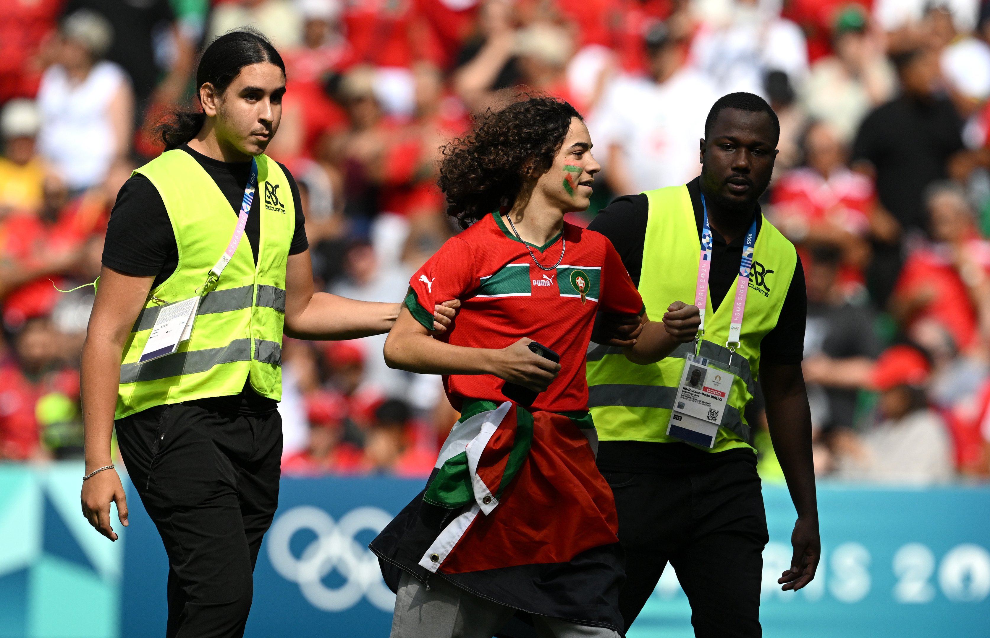 Comissários removem um invasor do campo durante a partida do grupo B masculino entre Argentina e Marrocos durante os Jogos Olímpicos de Paris 2024 no Stade Geoffroy-Guichard em 24 de julho de 2024 em Saint-Etienne, França.