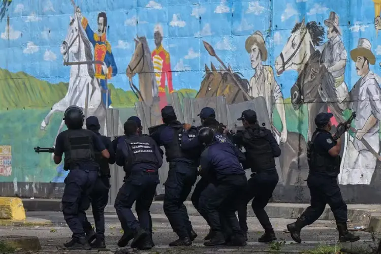 Com mural de Simon Bolívar ao fundo, policiais enfrentam manifestantes em rua de Caracas  (Yuri CORTEZ/AFP)