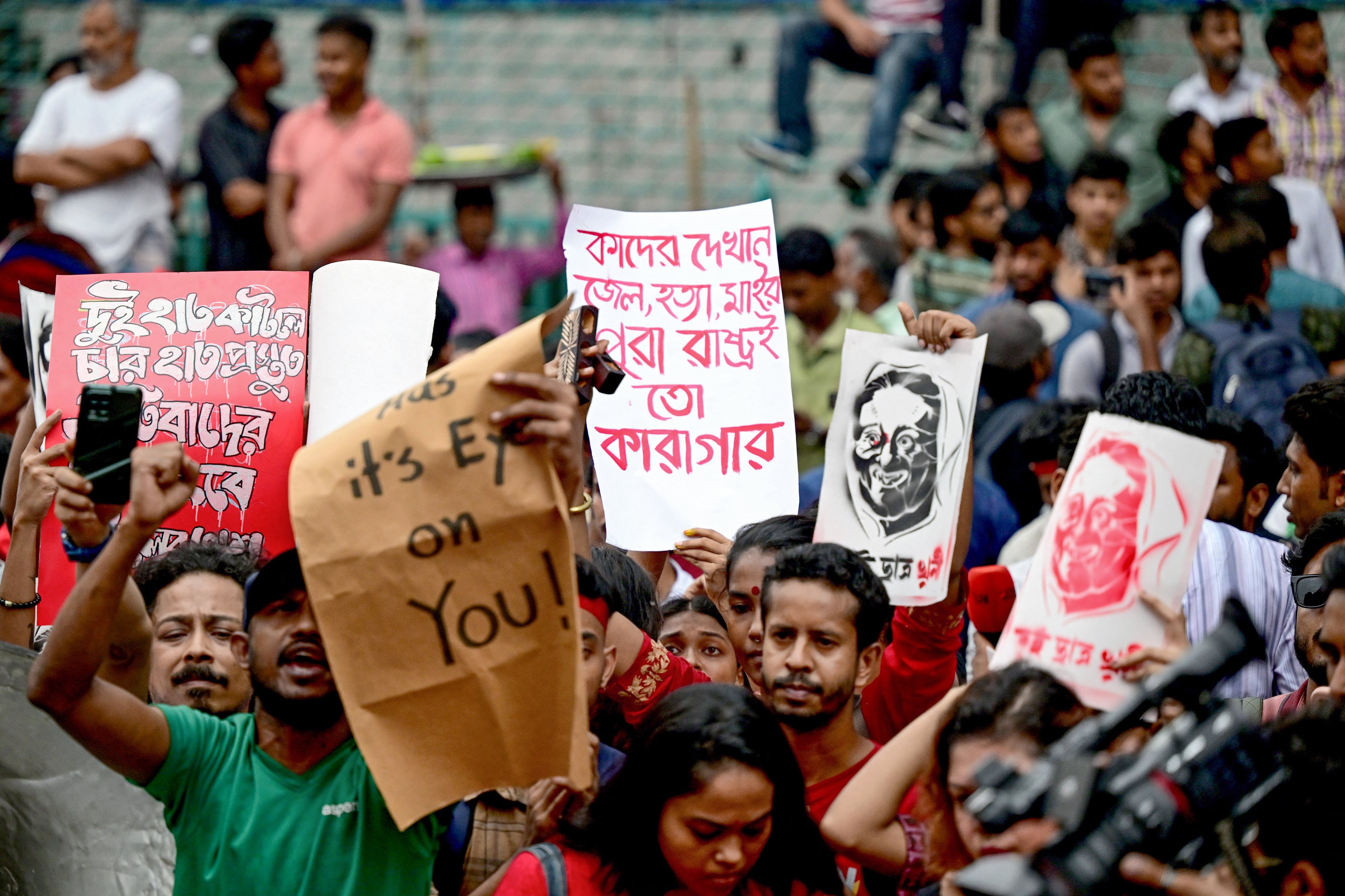 Ativistas culturais e membros da sociedade civil seguram cartazes retratando a primeira-ministra de Bangladesh, Sheikh Hasina, enquanto encenam uma marcha musical pelas vítimas que foram mortas durante os recentes protestos estudantis nacionais sobre cotas em empregos públicos, em Dhaka, em 30 de julho de 2024. O governo de Bangladesh convocou um dia de luto em 30 de julho pelas vítimas de violência em distúrbios nacionais, mas os estudantes denunciaram o gesto como desrespeitoso aos colegas de classe mortos durante confrontos com a polícia neste mês