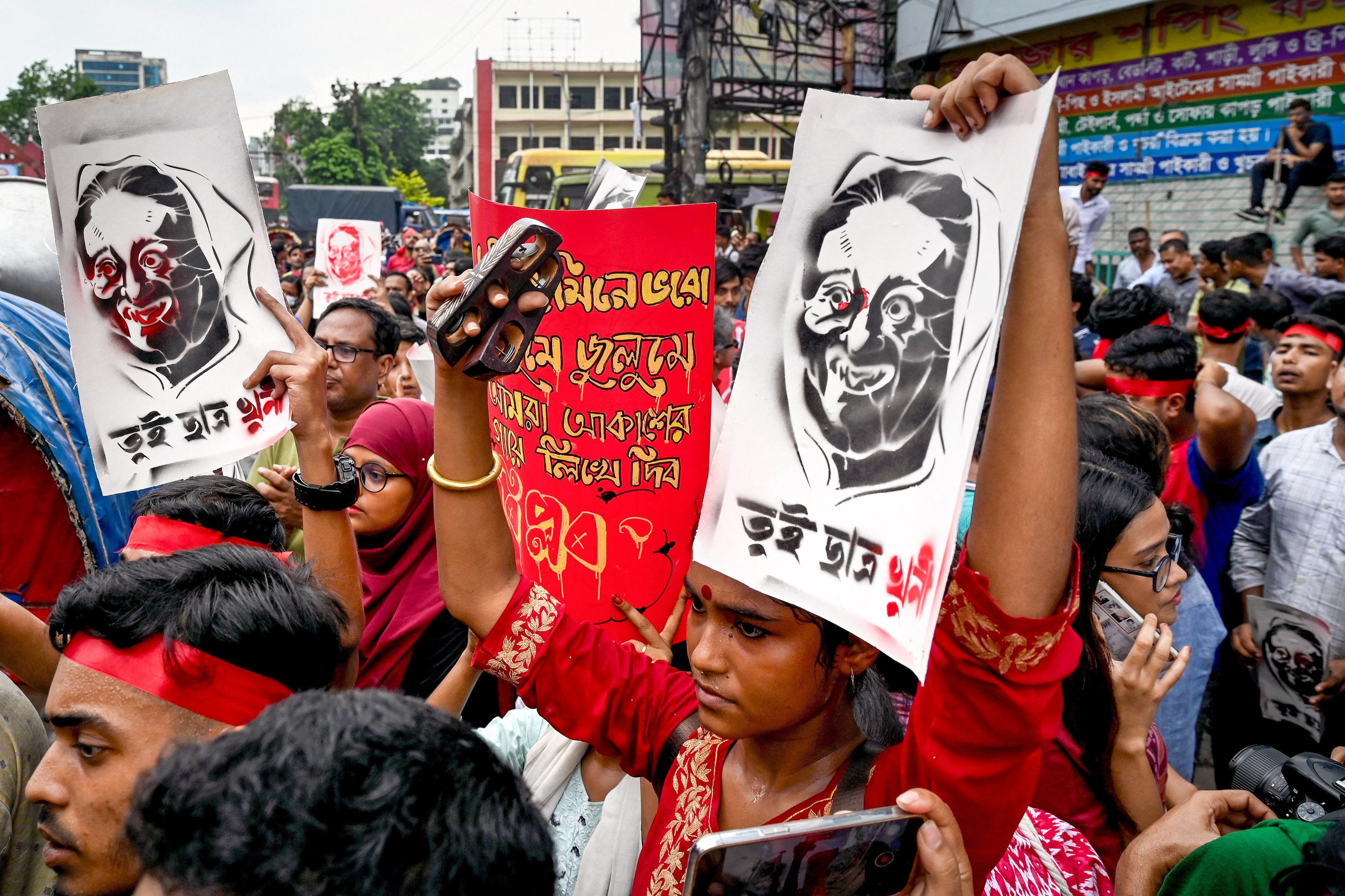 Ativistas culturais e membros da sociedade civil seguram cartazes retratando a primeira-ministra de Bangladesh, Sheikh Hasina, durante uma marcha musical pelas vítimas que foram mortas durante os recentes protestos estudantis nacionais sobre cotas em empregos públicos, em Dhaka, em 30 de julho de 2024. O governo de Bangladesh convocou um dia de luto em 30 de julho pelas vítimas da violência em distúrbios nacionais, mas os estudantes denunciaram o gesto como desrespeitoso aos colegas de classe mortos durante confrontos com a polícia neste mês