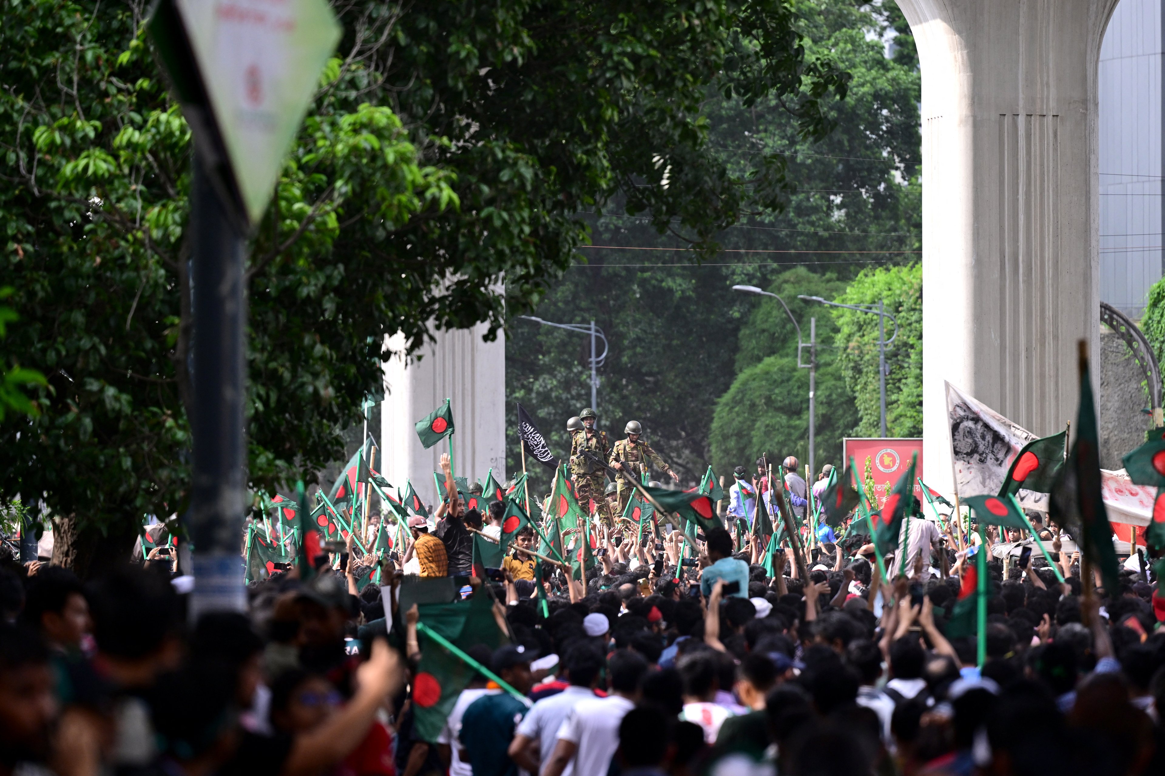 Manifestantes antigovernamentais marcham em direção ao palácio da primeira-ministra Sheikh Hasina enquanto militares (C) montam guarda na área de Shahbag, perto da universidade de Dhaka, em Dhaka, em 5 de agosto de 2024. Os protestos em Bangladesh, que começaram como manifestações lideradas por estudantes contra as regras de contratação do governo em julho, culminaram em 5 de agosto, com a fuga do primeiro-ministro e os militares anunciando que formariam um governo interino