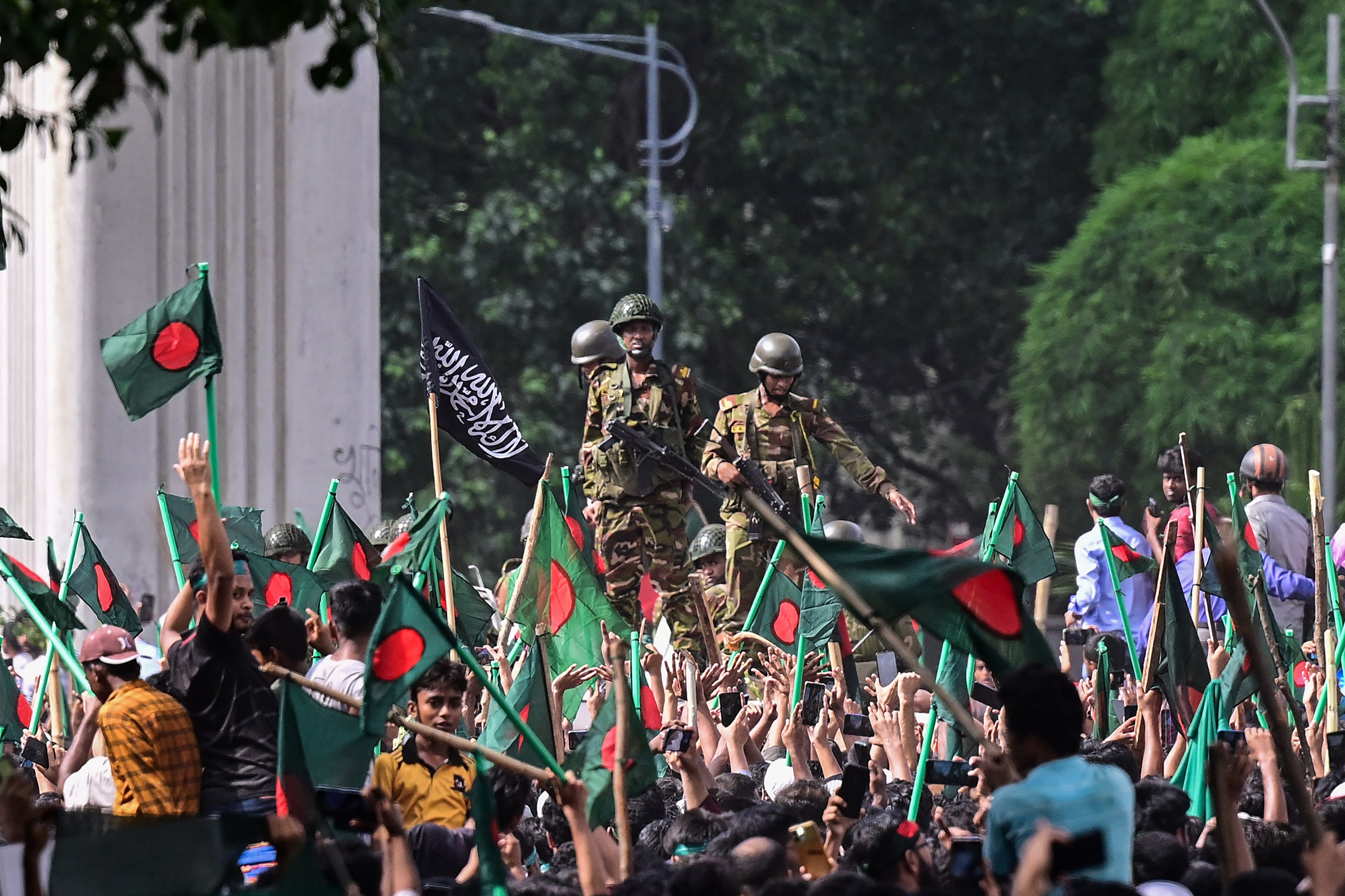Manifestantes antigovernamentais marcham em direção ao palácio da primeira-ministra Sheikh Hasina enquanto militares (C) montam guarda na área de Shahbag, perto da universidade de Dhaka, em Dhaka, em 5 de agosto de 2024. Os protestos em Bangladesh, que começaram como manifestações lideradas por estudantes contra as regras de contratação do governo em julho, culminaram em 5 de agosto, com a fuga do primeiro-ministro e os militares anunciando que formariam um governo interino
