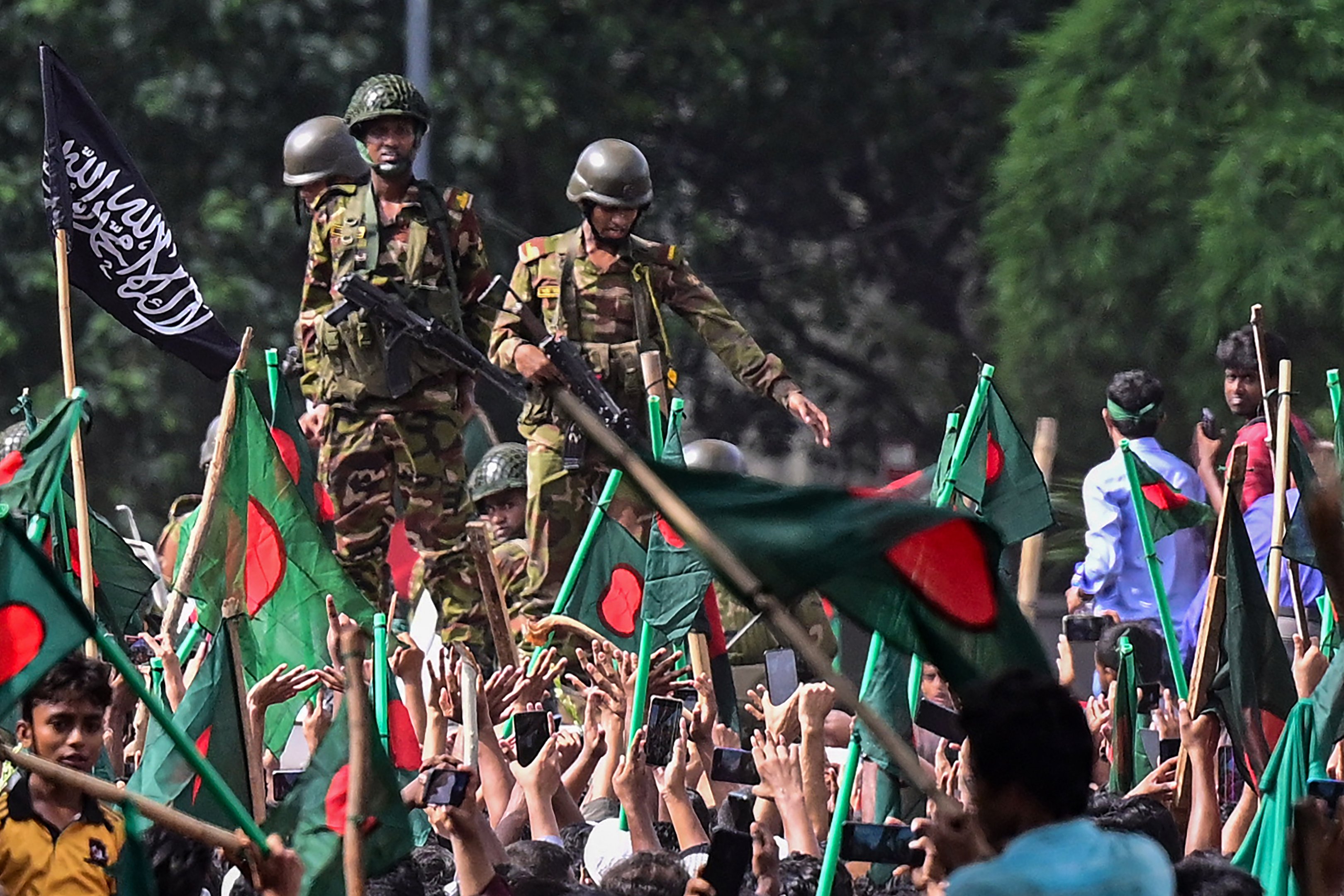 Manifestantes antigovernamentais marcham em direção ao palácio da primeira-ministra Sheikh Hasina enquanto militares (C) montam guarda na área de Shahbag, perto da universidade de Dhaka, em Dhaka, em 5 de agosto de 2024. Os protestos em Bangladesh, que começaram como manifestações lideradas por estudantes contra as regras de contratação do governo em julho, culminaram em 5 de agosto, com a fuga da primeira-ministra e o anúncio dos militares de que formariam um governo interino