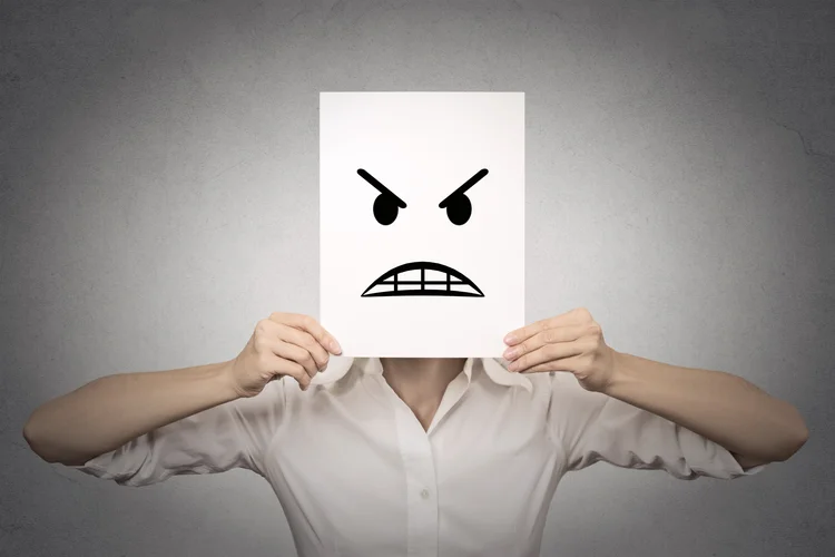 businesswoman covering her face with angry mask isolated grey wall background. Negative emotions, feelings, expressions, body language (AdobeStock)