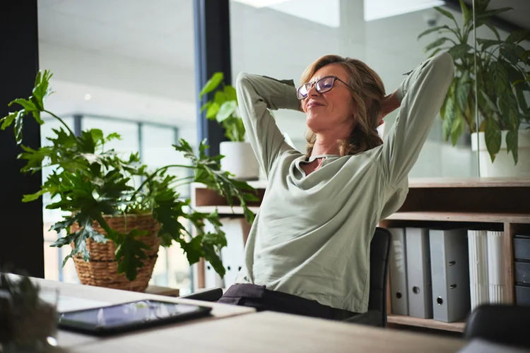 Sleep, relax and business woman finished with working on a project in office. Success, peace and calm with happy person resting after job complete, hands behind head and stretching for zen in company (DMP/Getty Images)