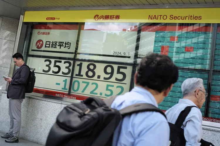 Homem passa por painel que mostra negociações do Nikkei 225 ((Photo by Kazuhiro NOGI / AFP))