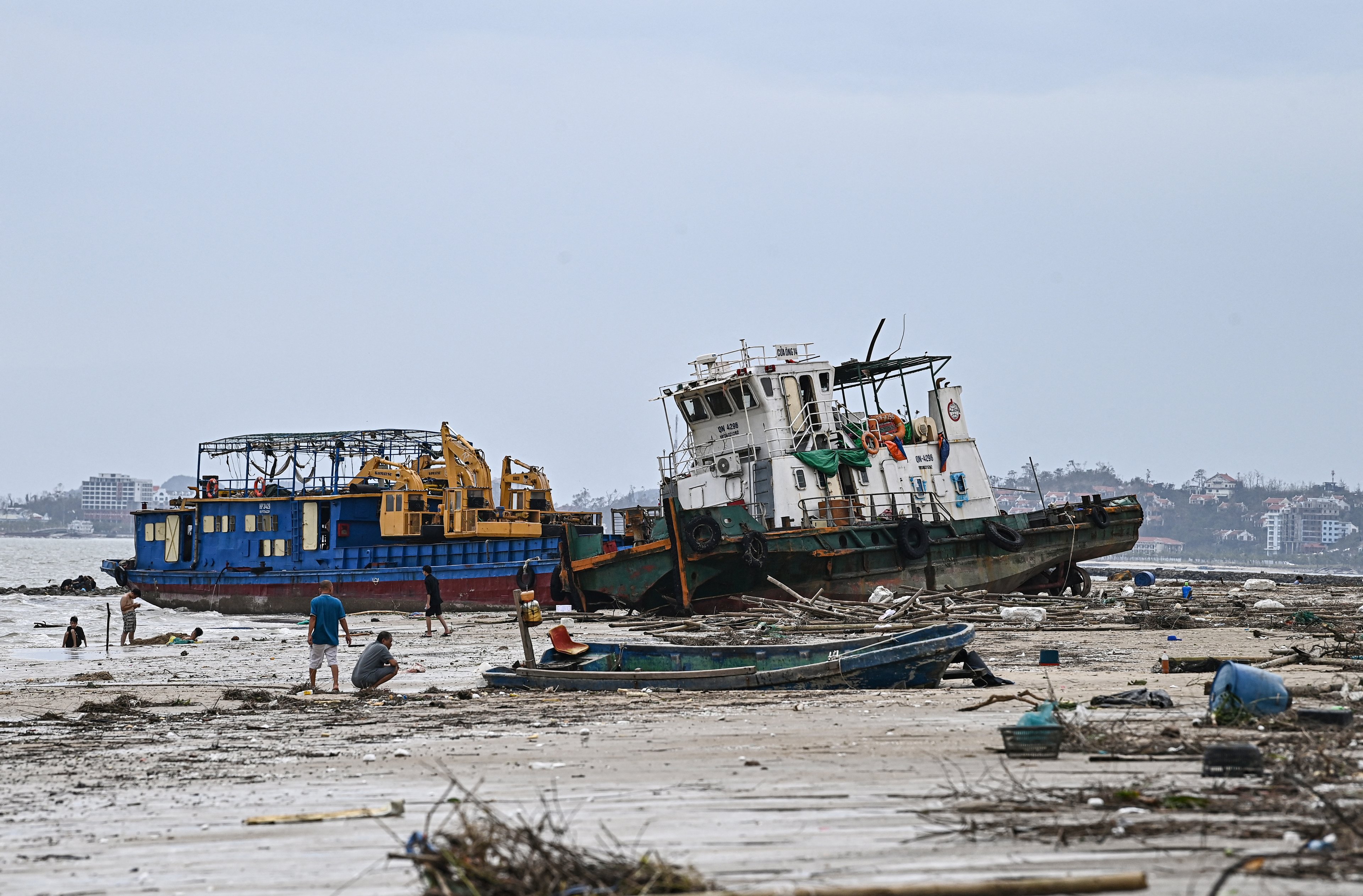 Pessoas inspecionam barcos danificados na praia de Bai Chay após o Super Tufão Yagi atingir Ha Long, na província de Quang Ninh, em 8 de setembro de 2024. O Super Tufão Yagi arranca milhares de árvores, varre navios e barcos para o mar e arranca telhados de casas no norte do Vietnã, após deixar um rastro de destruição no sul da China e nas Filipinas