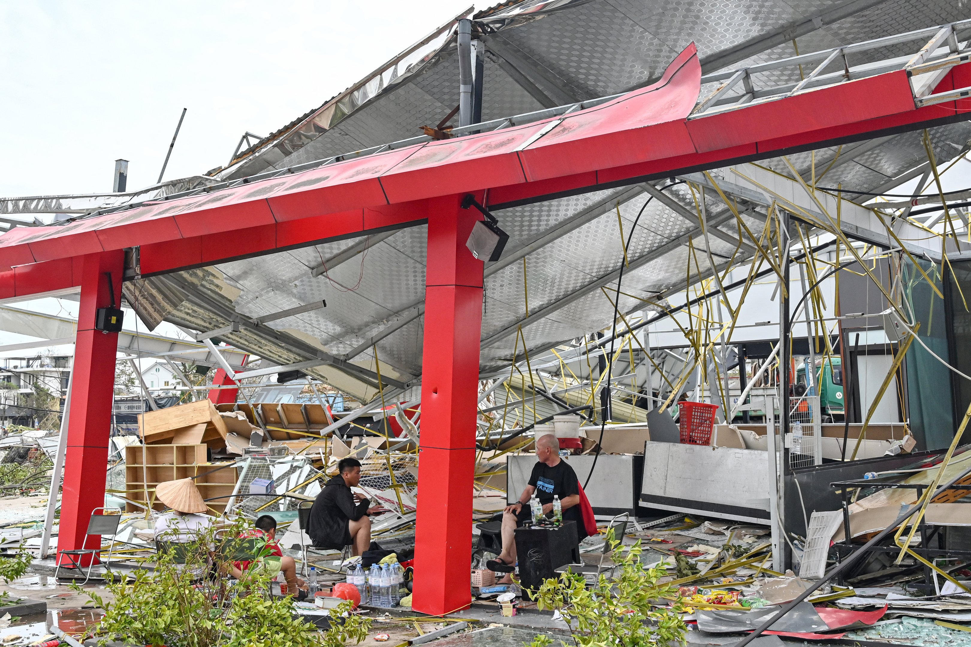 Pessoas sentam-se em meio aos destroços em um prédio destruído após o Super Tufão Yagi atingir Ha Long, na província de Quang Ninh, em 8 de setembro de 2024. O Super Tufão Yagi arranca milhares de árvores, varre navios e barcos para o mar e arranca telhados de casas no norte do Vietnã, após deixar um rastro de destruição no sul da China e nas Filipinas