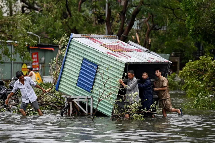 Homens coletam escombros em uma rua inundada após o Super Tufão Yagi atingir Hai Phong, em 8 de setembro de 2024. O Super Tufão Yagi arranca milhares de árvores, varre navios e barcos para o mar e arranca telhados de casas no norte do Vietnã, após deixar um rastro de destruição no sul da China e nas Filipinas (Nhac NGUYEN/AFP)