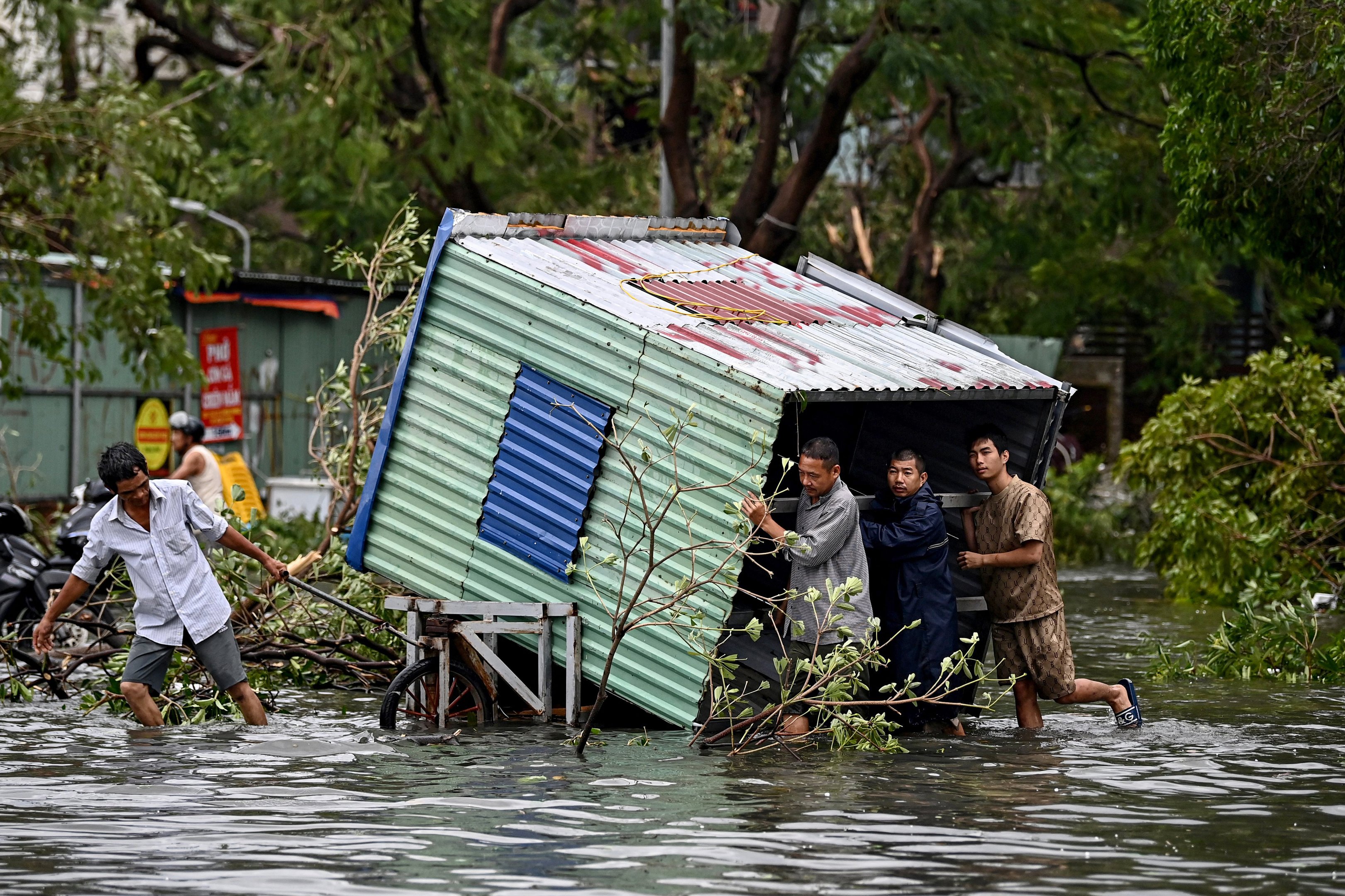 Homens coletam escombros em uma rua inundada após o Super Tufão Yagi atingir Hai Phong, em 8 de setembro de 2024. O Super Tufão Yagi arranca milhares de árvores, varre navios e barcos para o mar e arranca telhados de casas no norte do Vietnã, após deixar um rastro de destruição no sul da China e nas Filipinas