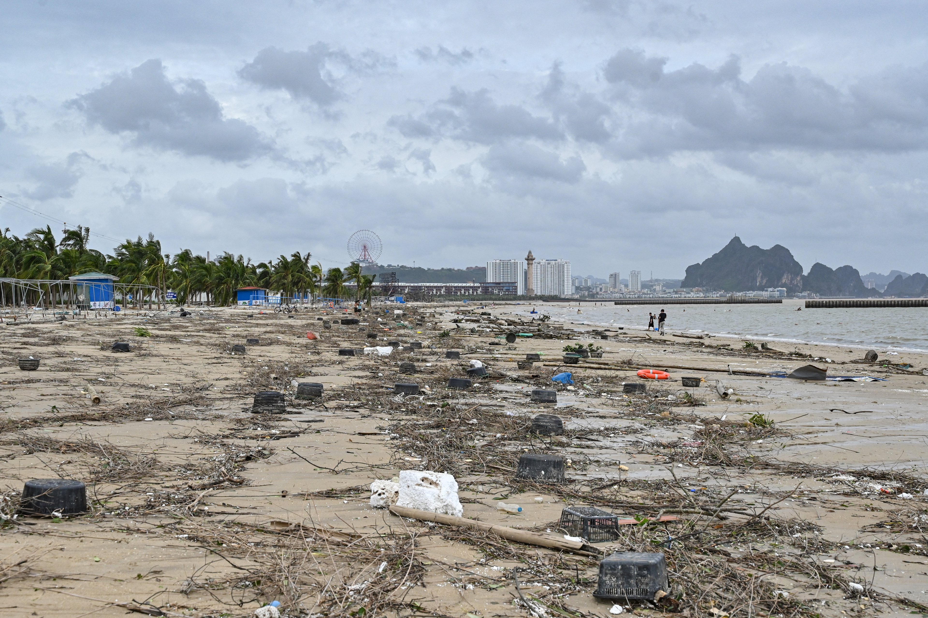 Pessoas caminham em meio aos destroços na praia de Bai Chay após o Super Tufão Yagi atingir Ha Long, na província de Quang Ninh, em 8 de setembro de 2024. O Super Tufão Yagi arranca milhares de árvores, varre navios e barcos para o mar e arranca telhados de casas no norte do Vietnã, após deixar um rastro de destruição no sul da China e nas Filipinas