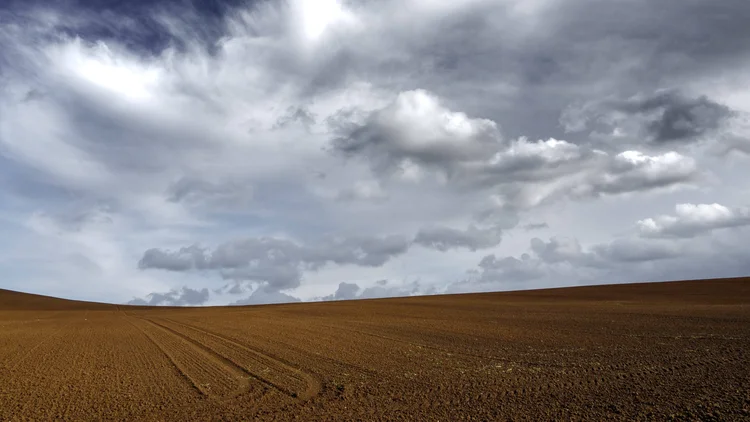 The brown sandy land under the dark cloudy grey sky (Freepik)