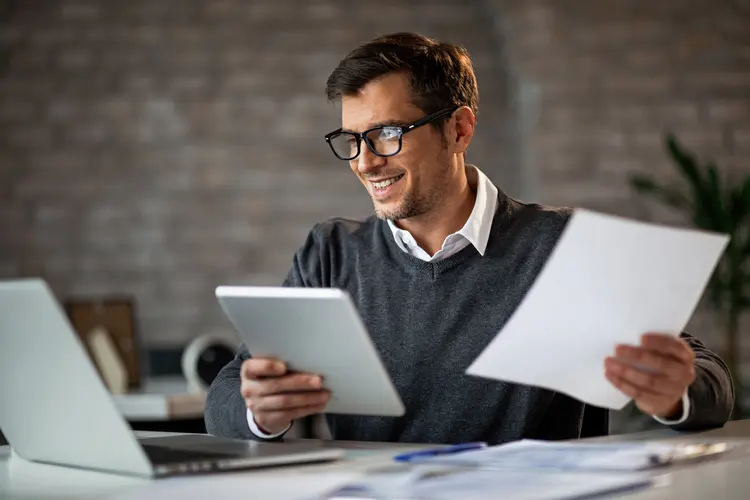 Happy businessman using touchpad and laptop while working on business reports in the office.