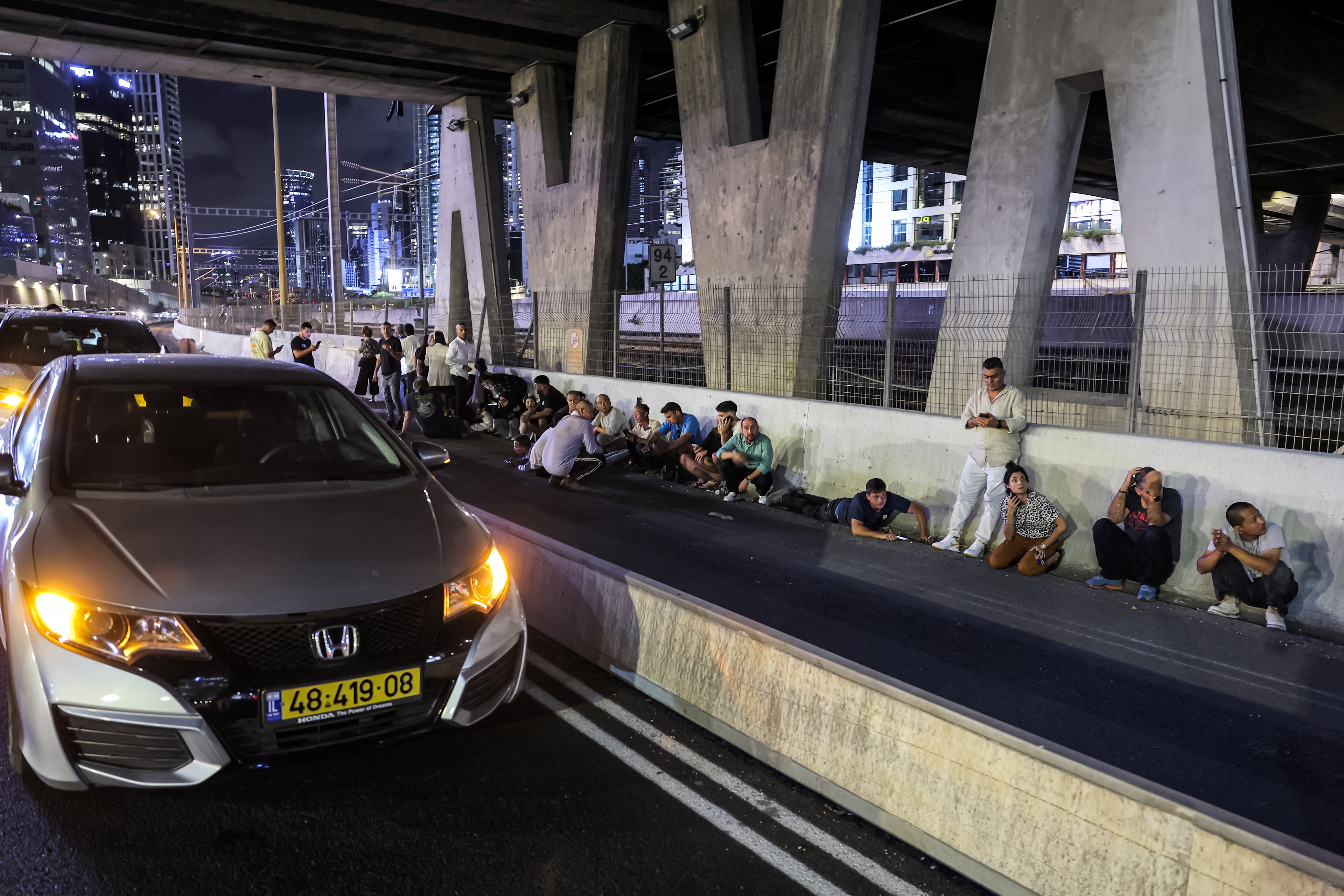 Pessoas se abrigam atrás de veículos sob uma ponte ao lado de uma rodovia em Tel Aviv, em 1º de outubro de 2024. Sirenes de ataque aéreo soaram no centro de Israel em 1º de outubro, informou o exército, um dia após o início das operações terrestres no sul do Líbano, visando posições do Hezbollah.