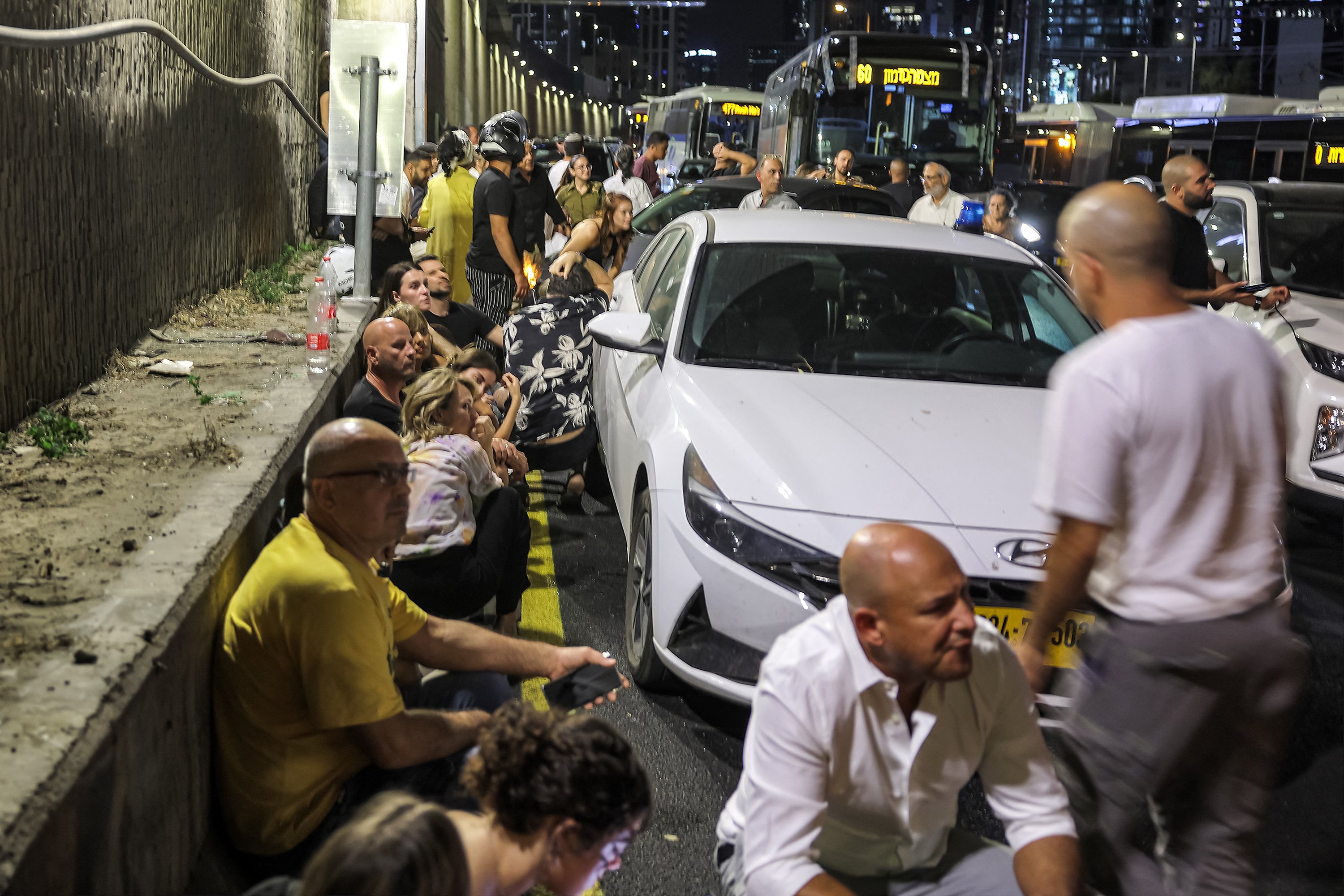 Pessoas se abrigam atrás de veículos sob uma ponte ao lado de uma rodovia em Tel Aviv, em 1º de outubro de 2024. Sirenes de ataque aéreo soaram no centro de Israel em 1º de outubro, informou o exército, um dia após o início das operações terrestres no sul do Líbano, visando posições do Hezbollah.