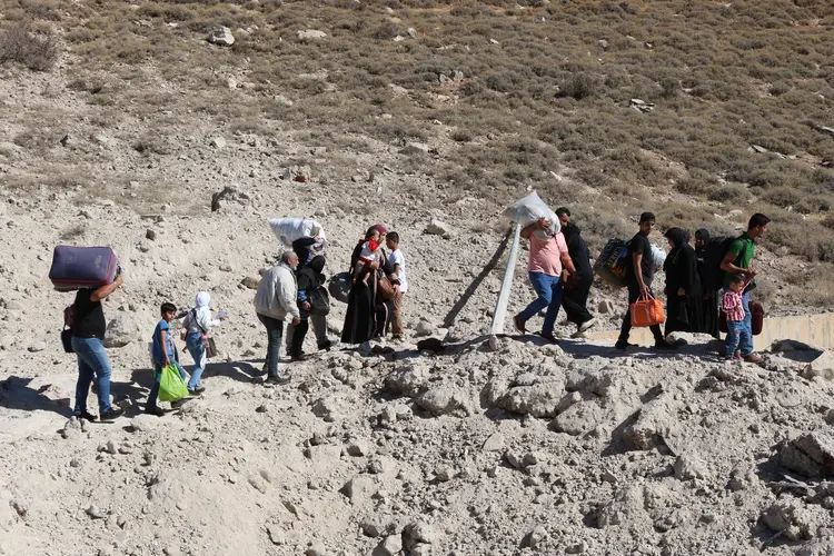 Pessoas fugindo do bombardeio israelense no Líbano, caminham ao redor de uma cratera causada por um ataque israelense, na área de Masnaa, no lado libanês da passagem de fronteira com a Síria, em 4 de outubro de 2024 (HASSAN JARRAH/AFP)