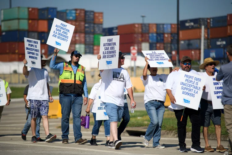 Trabalhadores em greve seguram cartazes e marcham em frente ao Terminal de Contêineres de Bayport em Seabrook, Texas, em 3 de outubro de 2024. A Associação Internacional de Estivadores (ILA), com 85.000 membros, lançou sua primeira greve desde 1977, após semanas de impasse nas negociações sobre um acordo de trabalho de seis anos (Mark Felix/AFP)