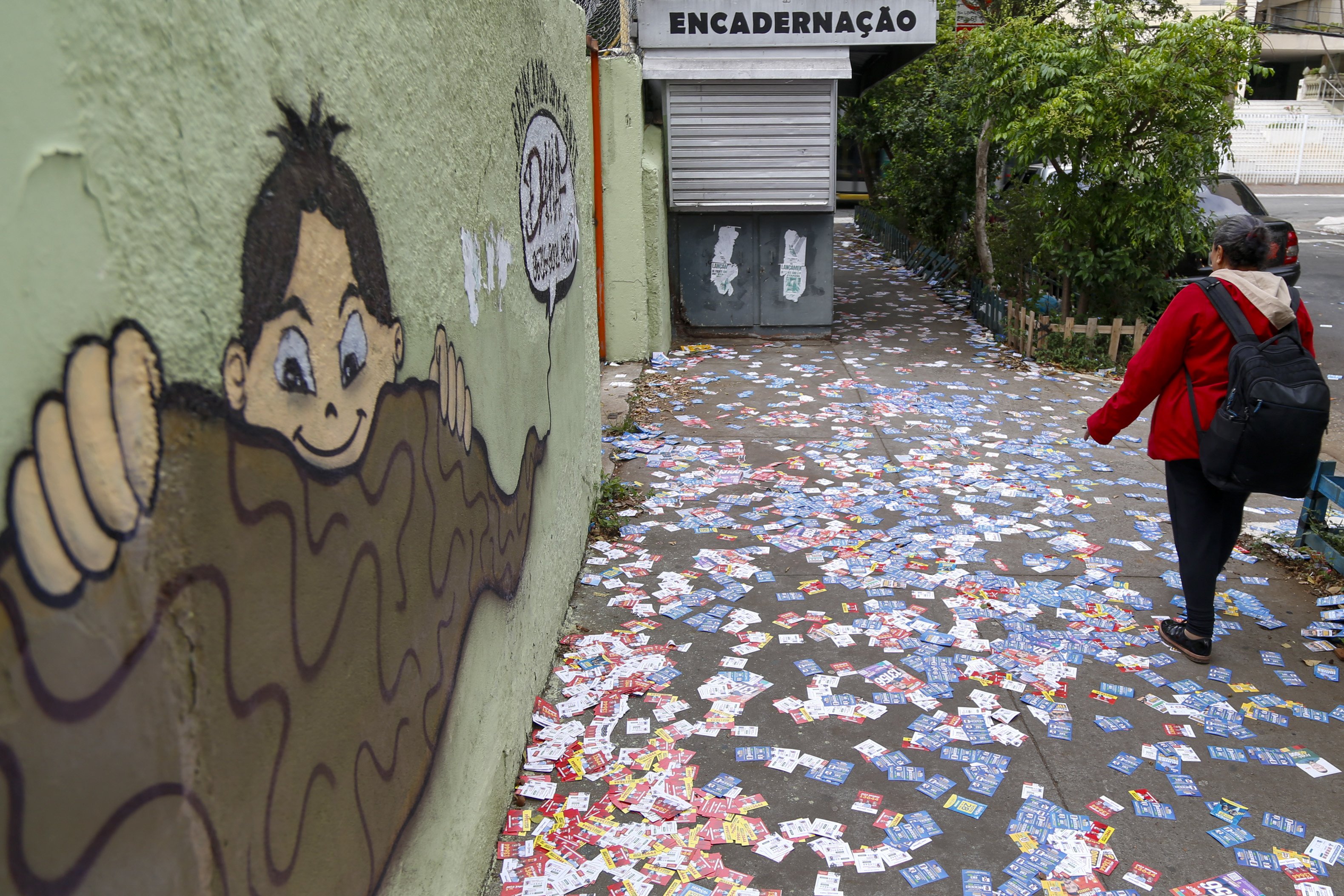 A woman walks along a pavement covered in ballot papers during the municipal elections first round, in Sao Paulo, Brazil, on October 6, 2024. Brazilians go to the polls Sunday to elect mayors and councillors in more than 5,500 cities after a vitriolic, sometimes violent campaign two years after presidential elections that polarized Latin America's biggest country. (Photo by Miguel SCHINCARIOL / AFP)