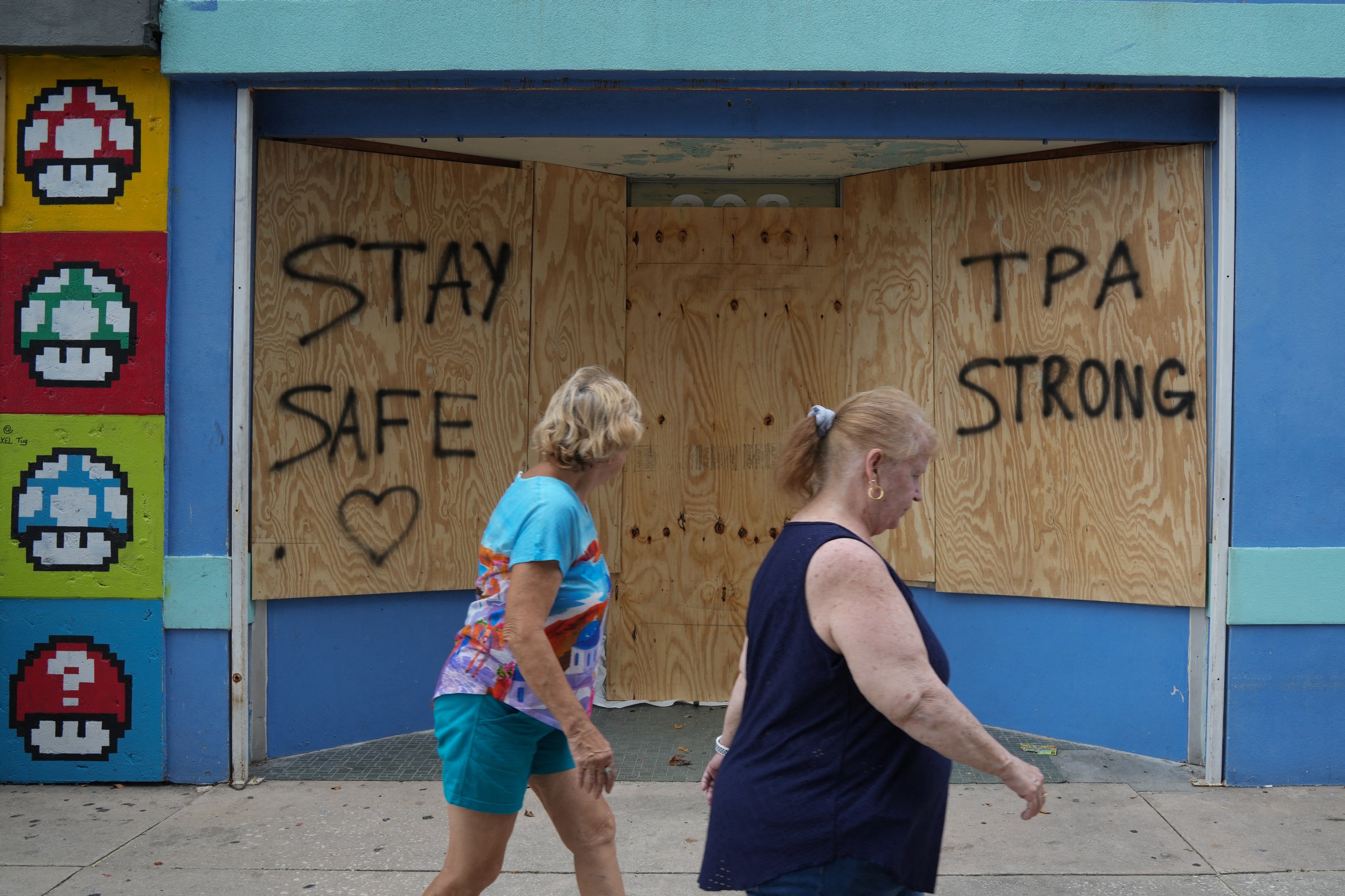 Pessoas passam por vitrines fechadas em Tampa antes do furacão Milton atingir a costa no meio desta semana, em 8 de outubro de 2024, na Flórida. O furacão Milton explodiu em força em 7 de outubro para se tornar uma tempestade de categoria 5 potencialmente catastrófica com destino à Flórida, ameaçando o estado dos EUA com um segundo furacão feroz em algumas semanas