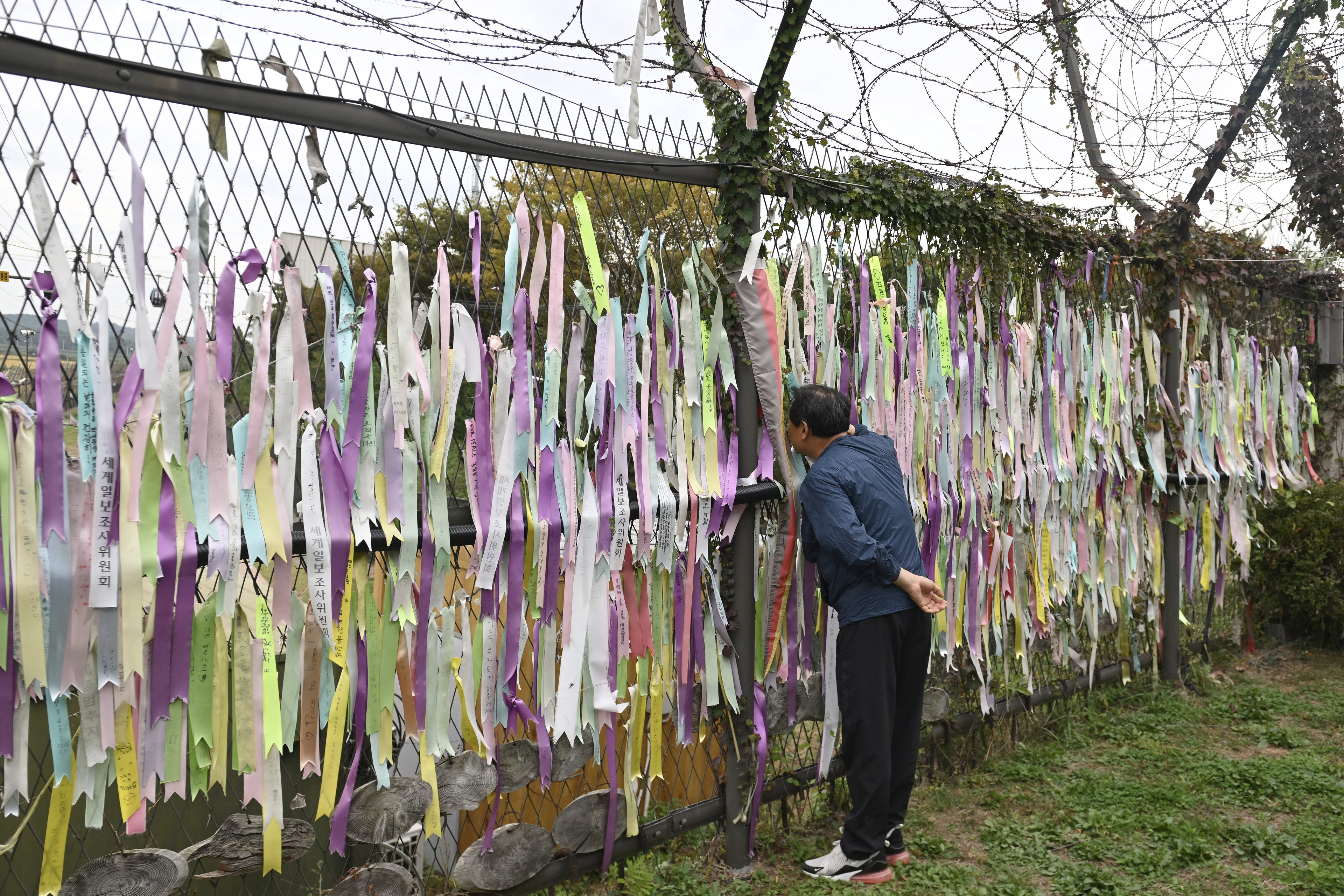 Um homem olha para fitas desejando paz e reunificação da Península Coreana penduradas em uma cerca militar no parque da paz Imjingak, perto da Zona Desmilitarizada (DMZ) que divide as duas Coreias em Paju, em 14 de outubro de 2024. Os militares da Coreia do Sul disseram em 14 de outubro que estavam "totalmente prontos" para responder depois que a Coreia do Norte ordenou que as tropas na fronteira se preparassem para atirar em uma disputa crescente sobre voos de drones para Pyongyang