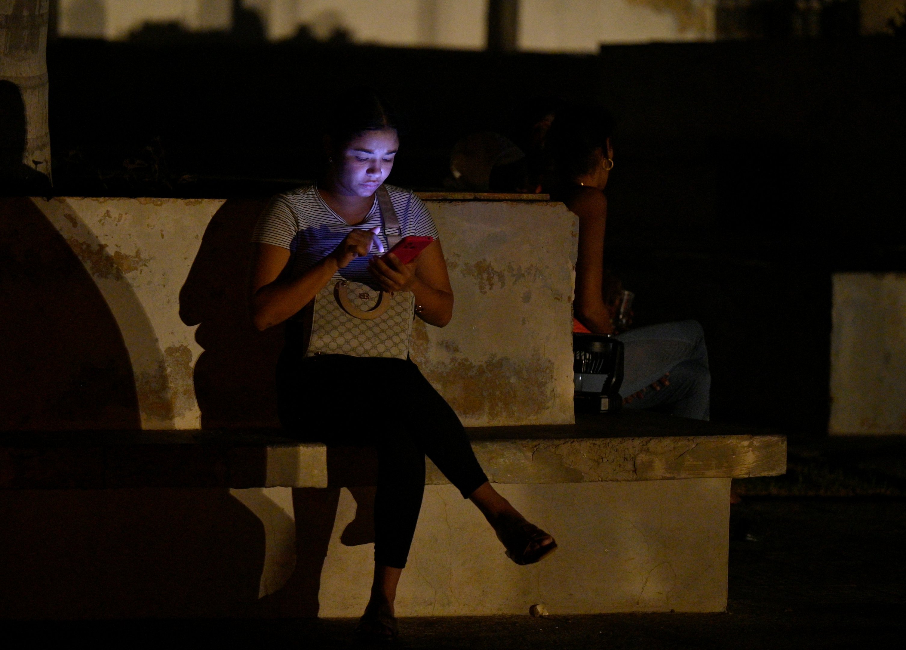 Uma mulher é iluminada por seu celular durante a terceira noite de um apagão nacional em Havana, em 20 de outubro de 2024. O presidente cubano Miguel Díaz-Canel alertou no domingo que agirá com 