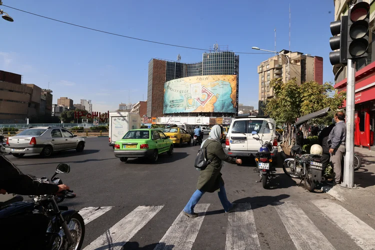 Pessoas caminham e dirigem em frente a um outdoor cobrindo a fachada de um prédio na praça Vali-Asr, em Teerã, em 26 de outubro de 2024 (Atta Kenare/AFP)