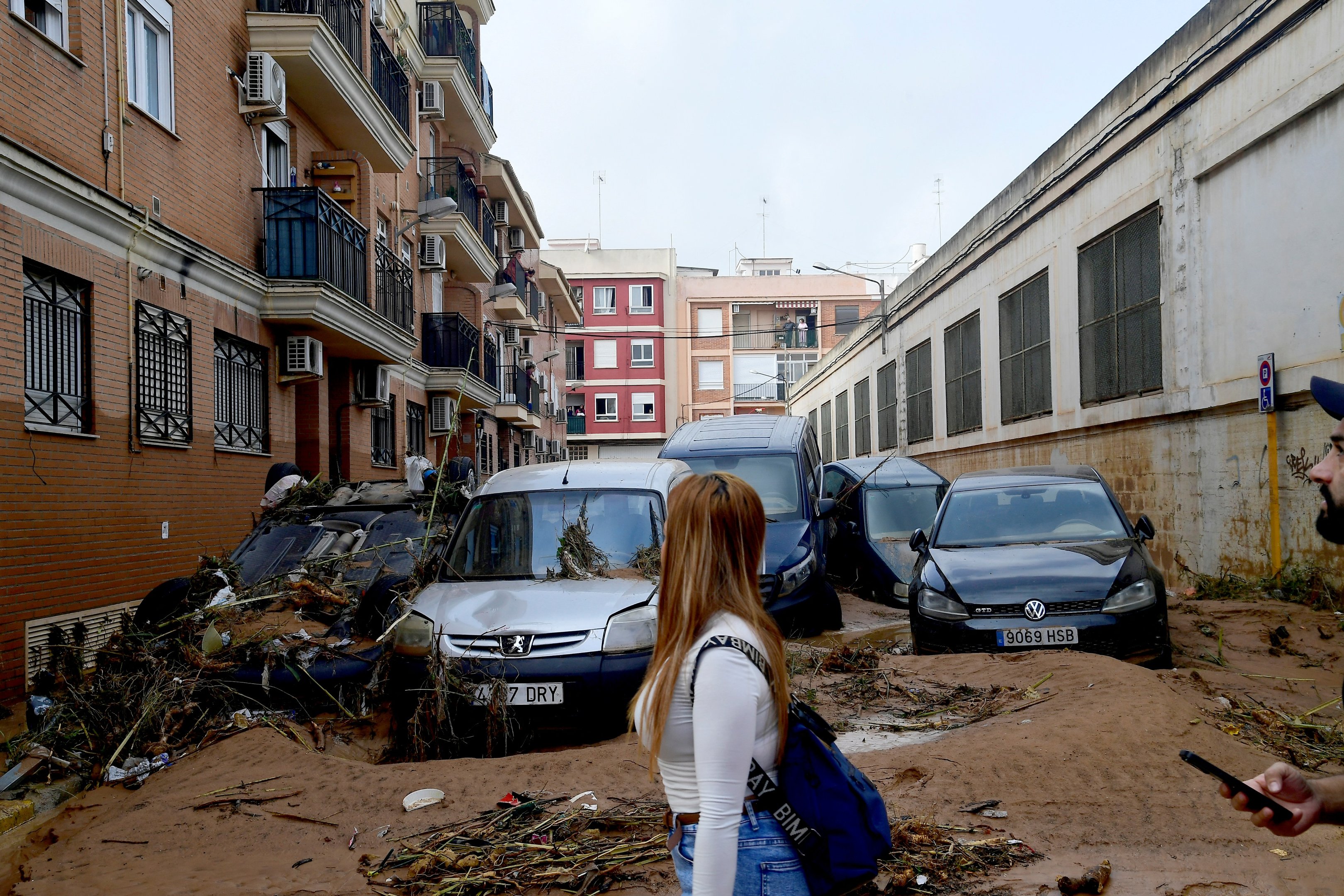 Pedestres caminham ao lado de carros empilhados em uma rua coberta de lama após enchentes em Picanya, perto de Valência, leste da Espanha, em 30 de outubro de 2024. Inundações provocadas por chuvas torrenciais na região de Valência, no leste da Espanha, deixaram 51 mortos, disseram serviços de resgate em outubro 30