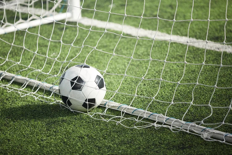 Leather soccer ball in empty gate behind net on green football field (Iancu Cojocar /Getty Images)