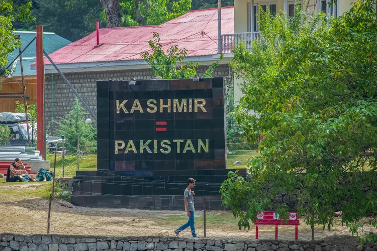 Um garoto na Caxemira administrada pelo Paquistão passa por uma placa que diz "Caxemira = Paquistão" instalada nas margens do rio Neelam ou Kishan Ganga  (Faisal Bashi/AFP)