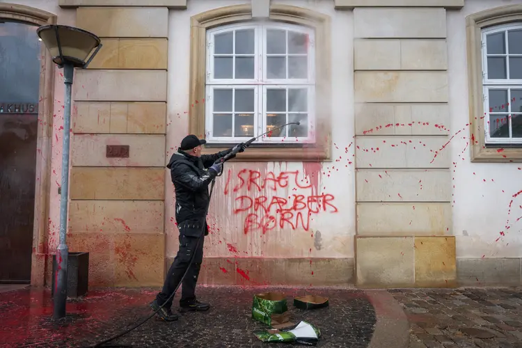 Um trabalhador usa uma mangueira de pressão para limpar a tinta vermelha e os slogans anti-Israel da fachada do prédio do Ministério das Relações Exteriores, Eigtveds Pakhus, em Copenhague, Dinamarca, em 26 de setembro de 2024 (EMIL NICOLAI HELMS/Getty Images)