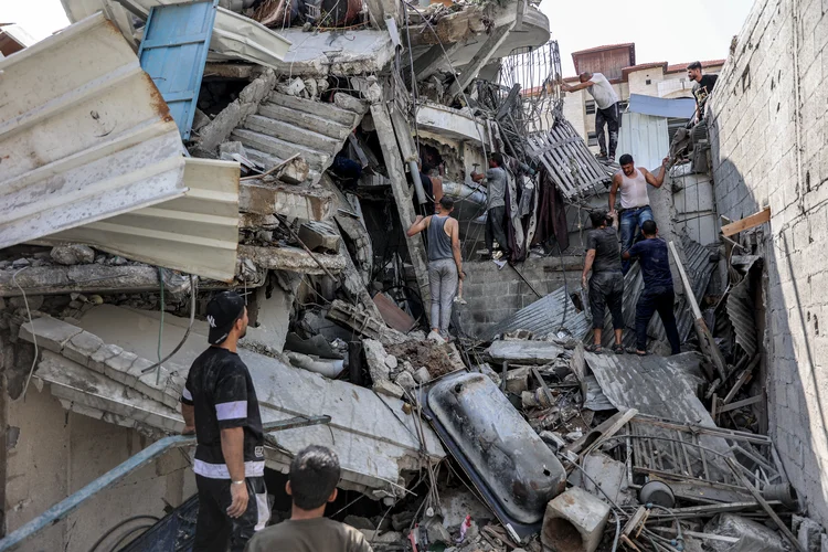 Pessoas se reúnem do lado de fora de um prédio desabado enquanto tentam resgatar um homem debaixo dos escombros após o bombardeio israelense no distrito de Saftawi em Jabalia, no norte da Faixa de Gaza, em 15 de outubro de 2024, em meio à guerra em curso no território palestino entre Israel e o Hamas (Omar AL-QATTAA/Getty Images)