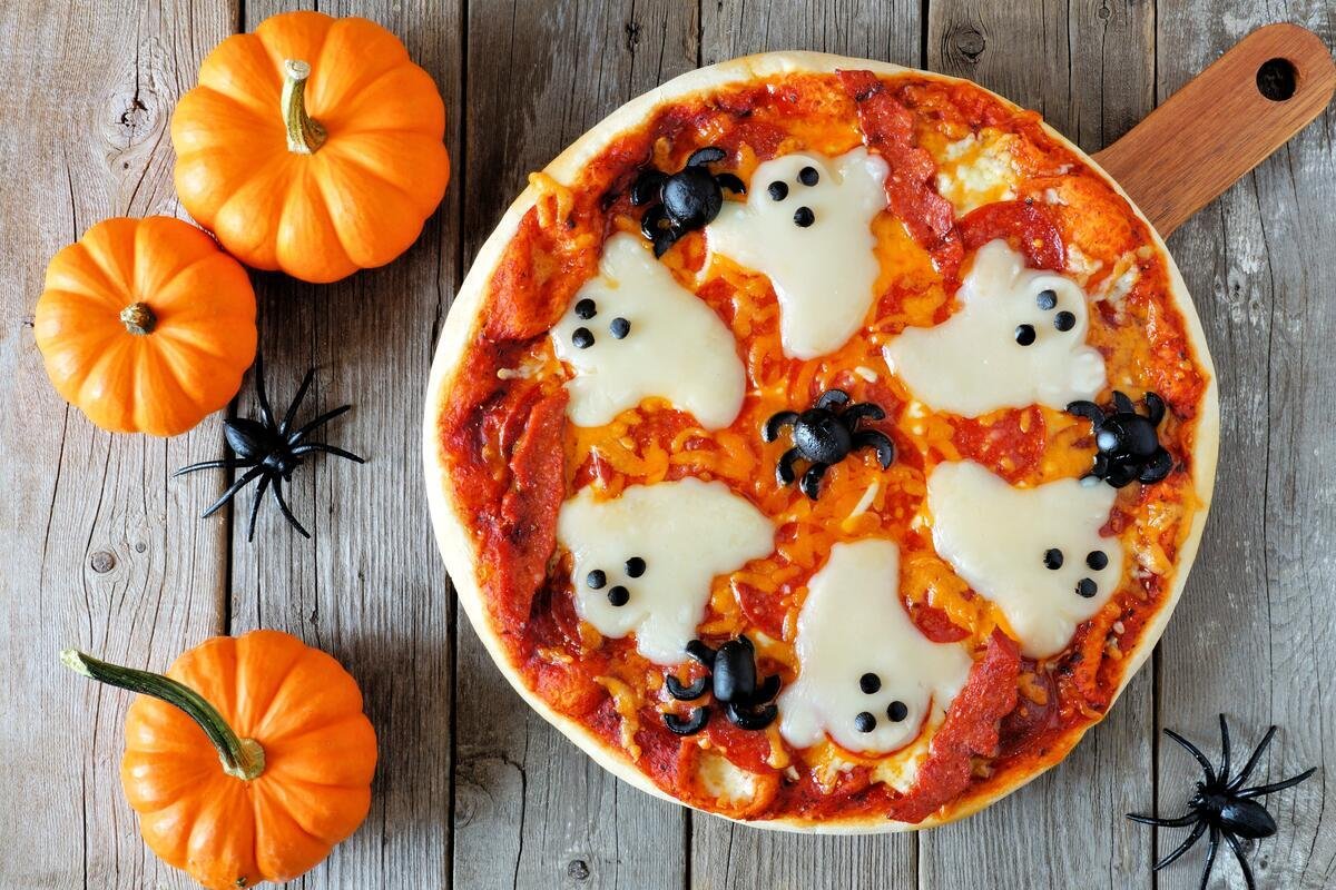 Halloween pizza with ghosts and spiders, above scene with decor on a rustic wood background