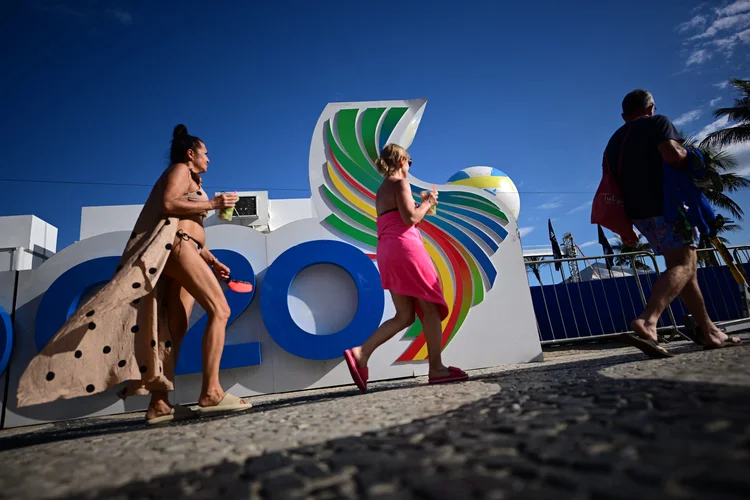 Banhistas passam por uma faixa da Cúpula do G20 na praia de Copacabana, Rio de Janeiro, Brasil, em 6 de novembro de 2024. A Cúpula dos Líderes do G20 acontecerá no Rio de Janeiro entre 18 e 19 de novembro de 2024 (Mauro PIMENTEL /AFP)