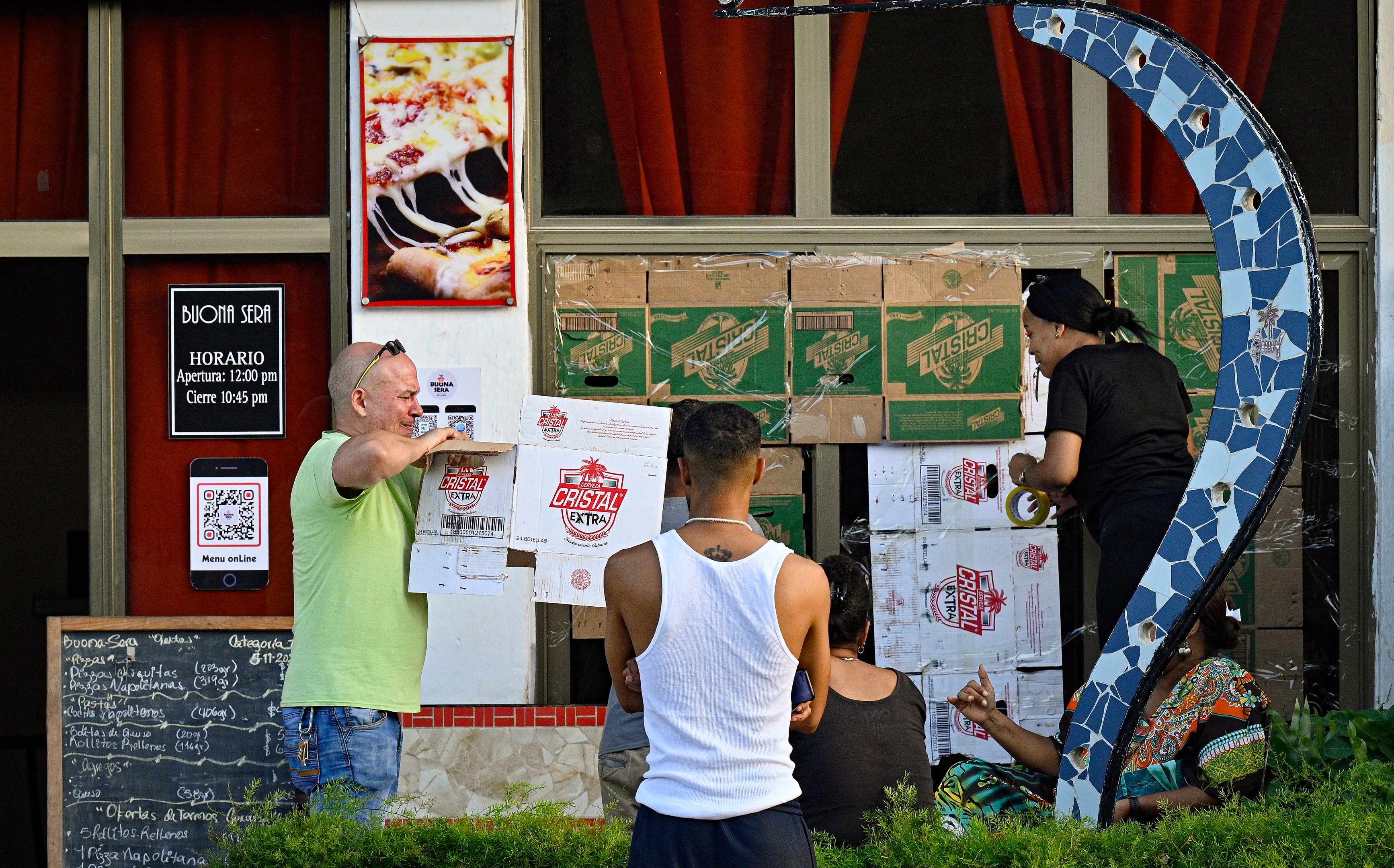 Pessoas protegem as janelas de um restaurante com papelão antes da chegada da tempestade tropical Rafael em Havana em 5 de novembro de 2024. Cuba estava se preparando para a tempestade tropical Rafael, que deve atingir a ilha como um furacão em 6 de novembro, agravando a miséria causada por um grande apagão e pelo furacão Oscar