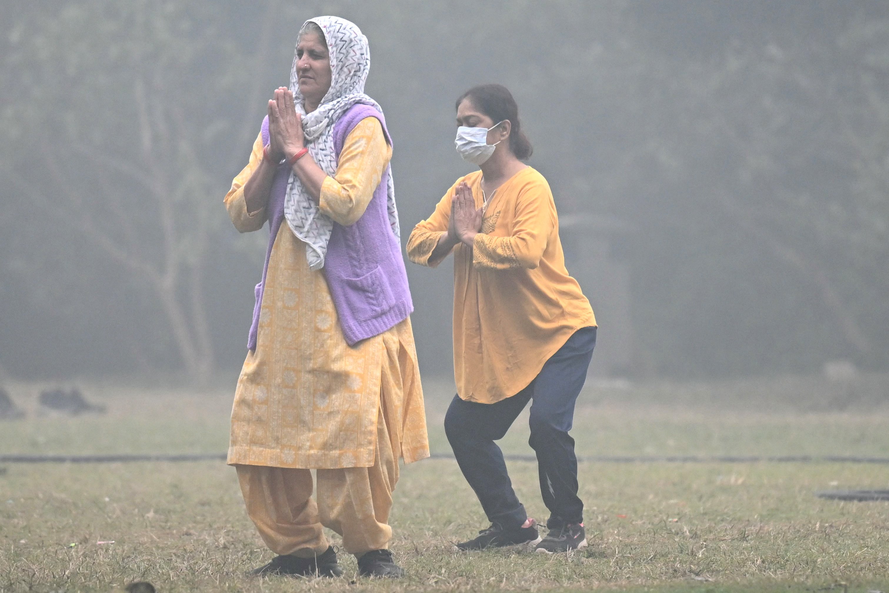 Mulheres usam máscaras enquanto se exercitam nos jardins de Lodhi em uma manhã fria e poluída em Nova Déli, em 18 de novembro de 2024. A capital da Índia, Nova Déli, mudou as escolas para aulas online em 18 de novembro até novo aviso devido ao agravamento da poluição tóxica, a mais recente tentativa de aliviar a crise de saúde da megacidade em expansão