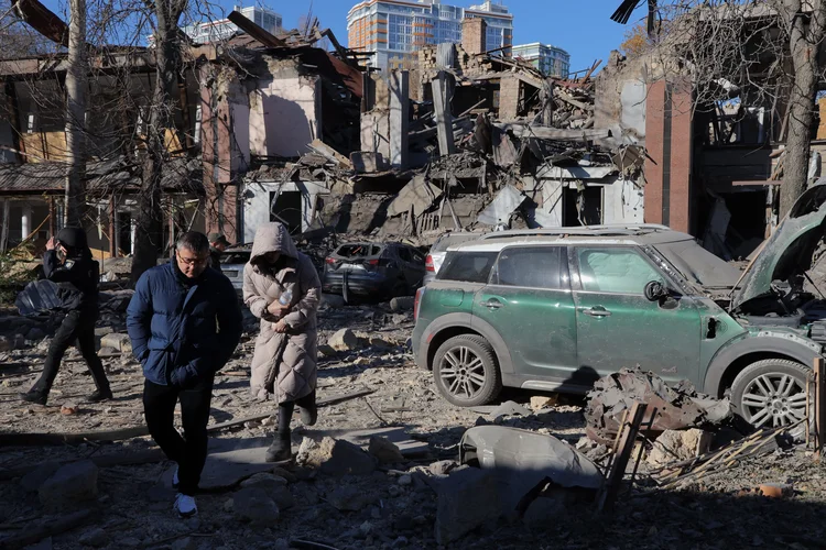 Moradores locais e um policial caminham ao lado de carros danificados no pátio de um prédio destruído após um ataque de mísseis em Odessa em 25 de novembro de 2024 (Oleksandr GIMANOV /AFP)