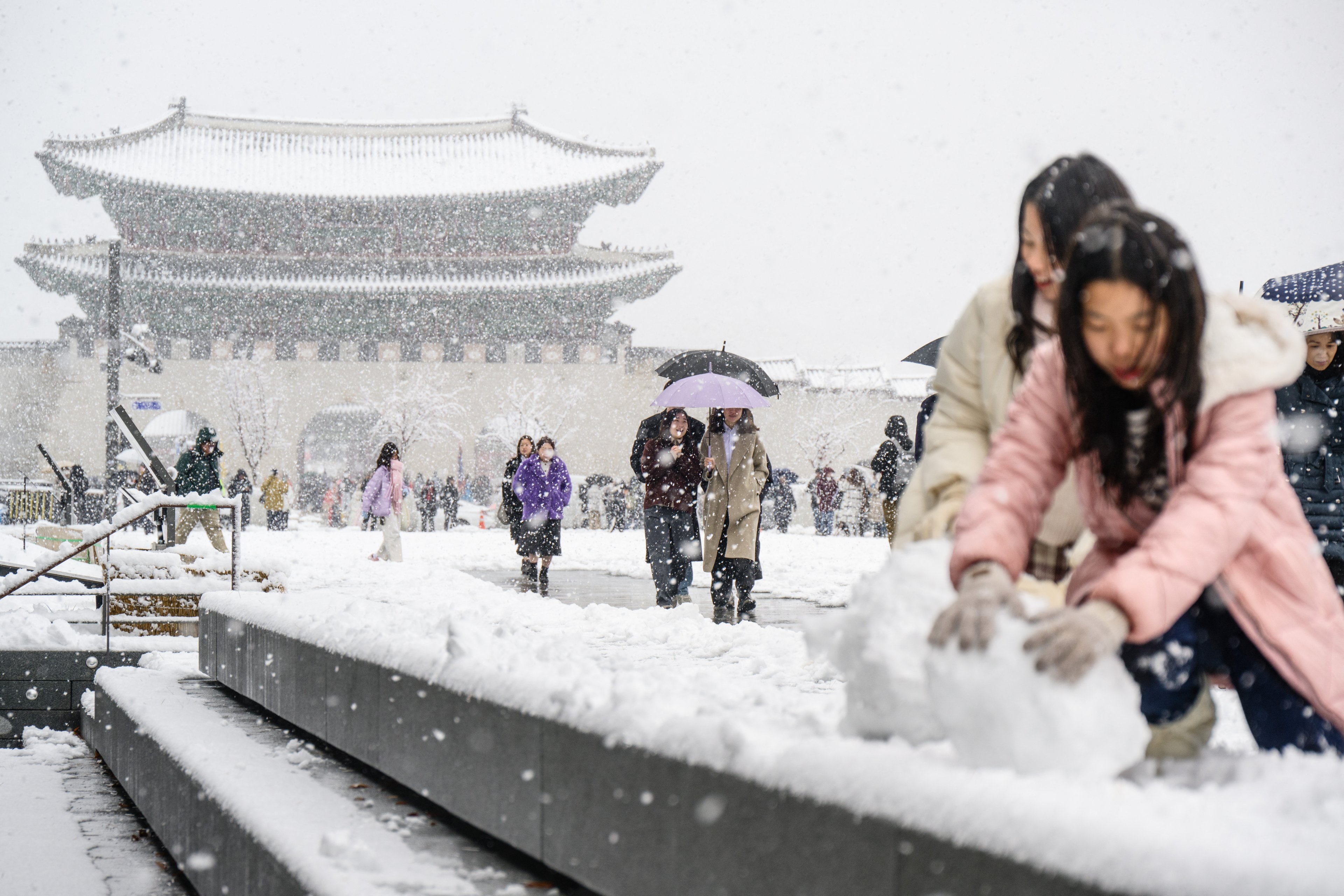 Pedestres caminham em frente ao Palácio Gyeongbokgung em meio a uma forte nevasca no centro de Seul em 27 de novembro de 2024. A capital da Coreia do Sul foi coberta em 27 de novembro pela maior nevasca de novembro desde que os registros começaram há mais de um século, disse a agência meteorológica