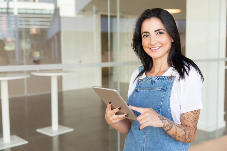 Content young woman holding digital tablet. Beautiful happy young woman using tablet computer and smiling at camera. Wireless technology concept