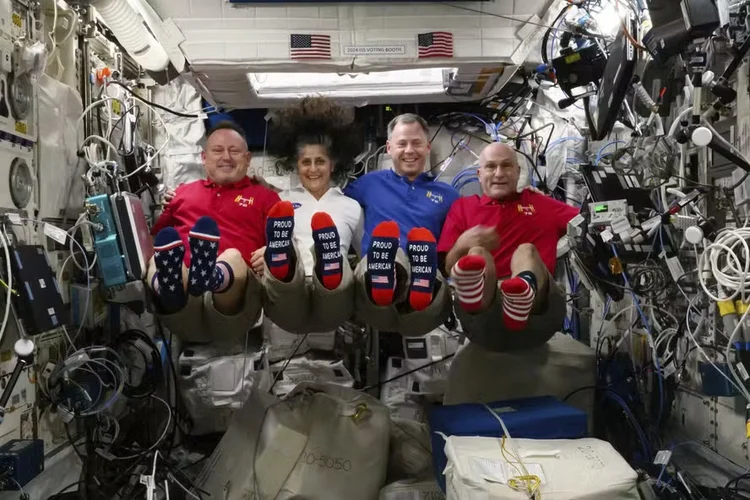 Da esquerda para a direita, os astronautas Butch Wilmore, Suni Williams, Nick Hague e Don Pettit exibem suas meias com tema da bandeira dos EUA