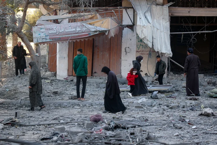 Palestinos caminham entre os escombros em frente a um prédio destruído em um ataque aéreo israelense em Nuseirat, no centro da Faixa de Gaza, em 1º de dezembro de 2024, enquanto a guerra entre Israel e militantes do Hamas continua (Eyad BABA/AFP)