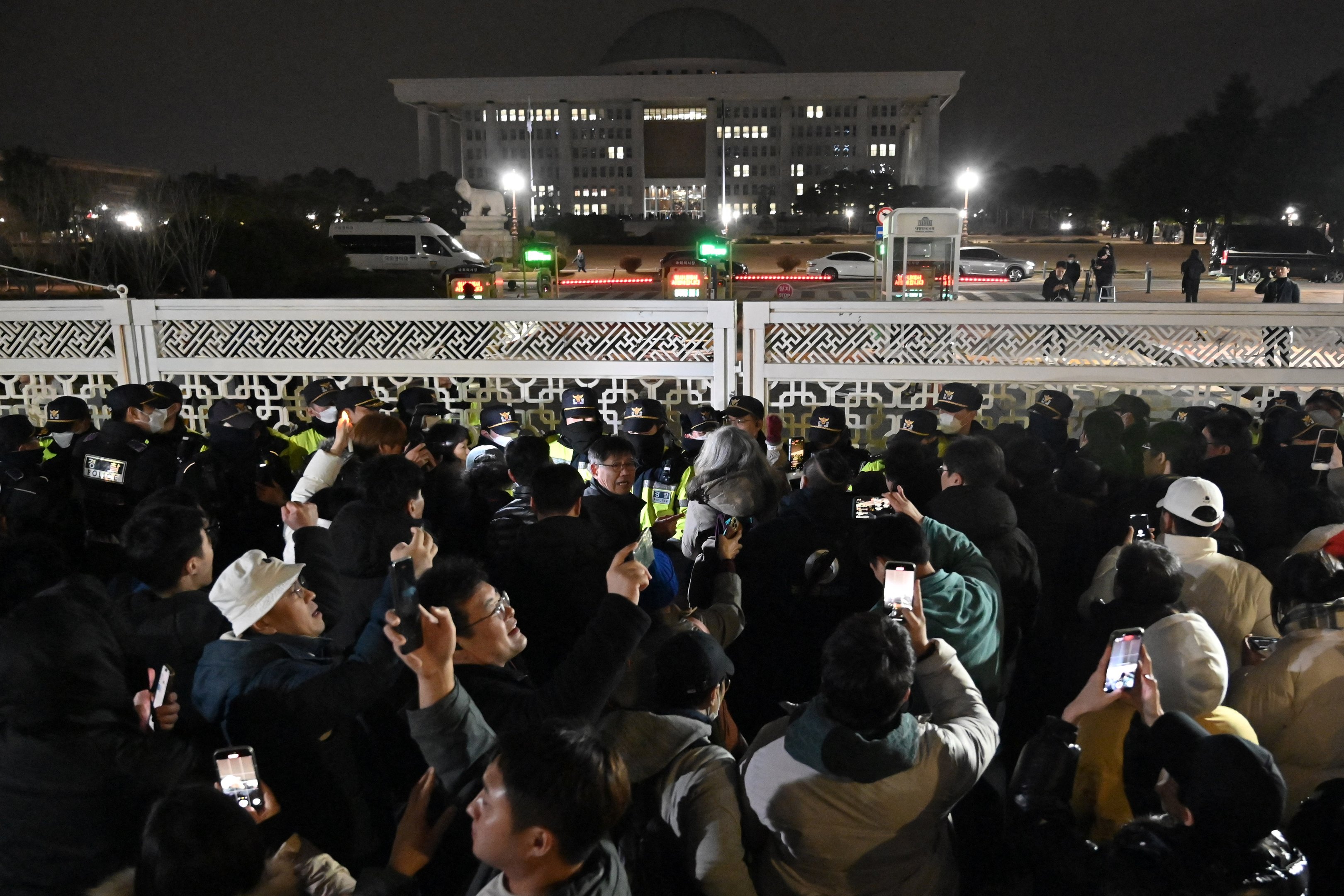 Pessoas se reúnem em frente ao portão principal da Assembleia Nacional em Seul, Coreia do Sul, em 4 de dezembro de 2024, depois que o presidente Yoon Suk Yeol declarou lei marcial de emergência. O presidente da Coreia do Sul, Yoon Suk Yeol, declarou lei marcial de emergência em 3 de dezembro, dizendo que a medida era necessária para proteger o país de "forças comunistas" em meio a disputas parlamentares sobre um projeto de lei orçamentária