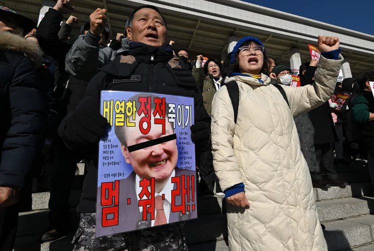 Membros do principal partido de oposição da Coreia do Sul, o Partido Democrático, seguram um cartaz mostrando uma foto danificada do presidente sul-coreano Yoon Suk Yeol durante um comício contra ele na Assembleia Nacional em Seul em 4 de dezembro de 2024 (JUNG YEON-JE/AFP)