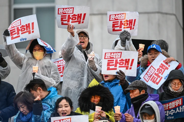 Manifestantes seguram cartazes com os dizeres "Yoon Suk Yeol impeachment!" durante um comício à luz de velas pedindo a deposição do presidente da Coreia do Sul, Yoon Suk Yeol, nos degraus da Assembleia Nacional em Seul, em 5 de dezembro de 2024 (JUNG Yeon-je/AFP)